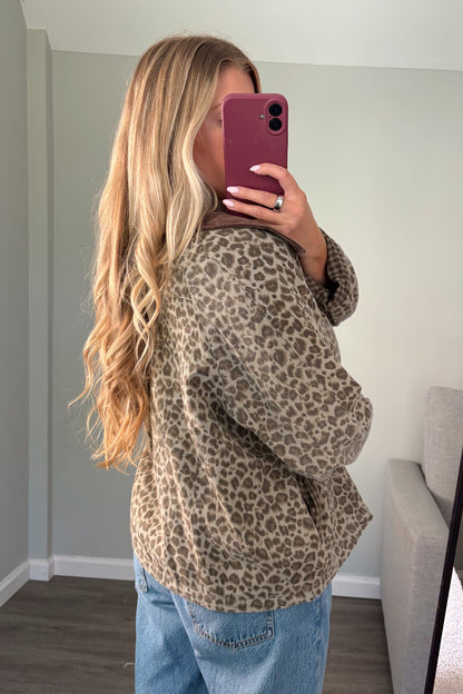 A woman takes a mirror selfie showing off a brown and beige leopard print fleece jacket, paired with light blue jeans in a home setting.
