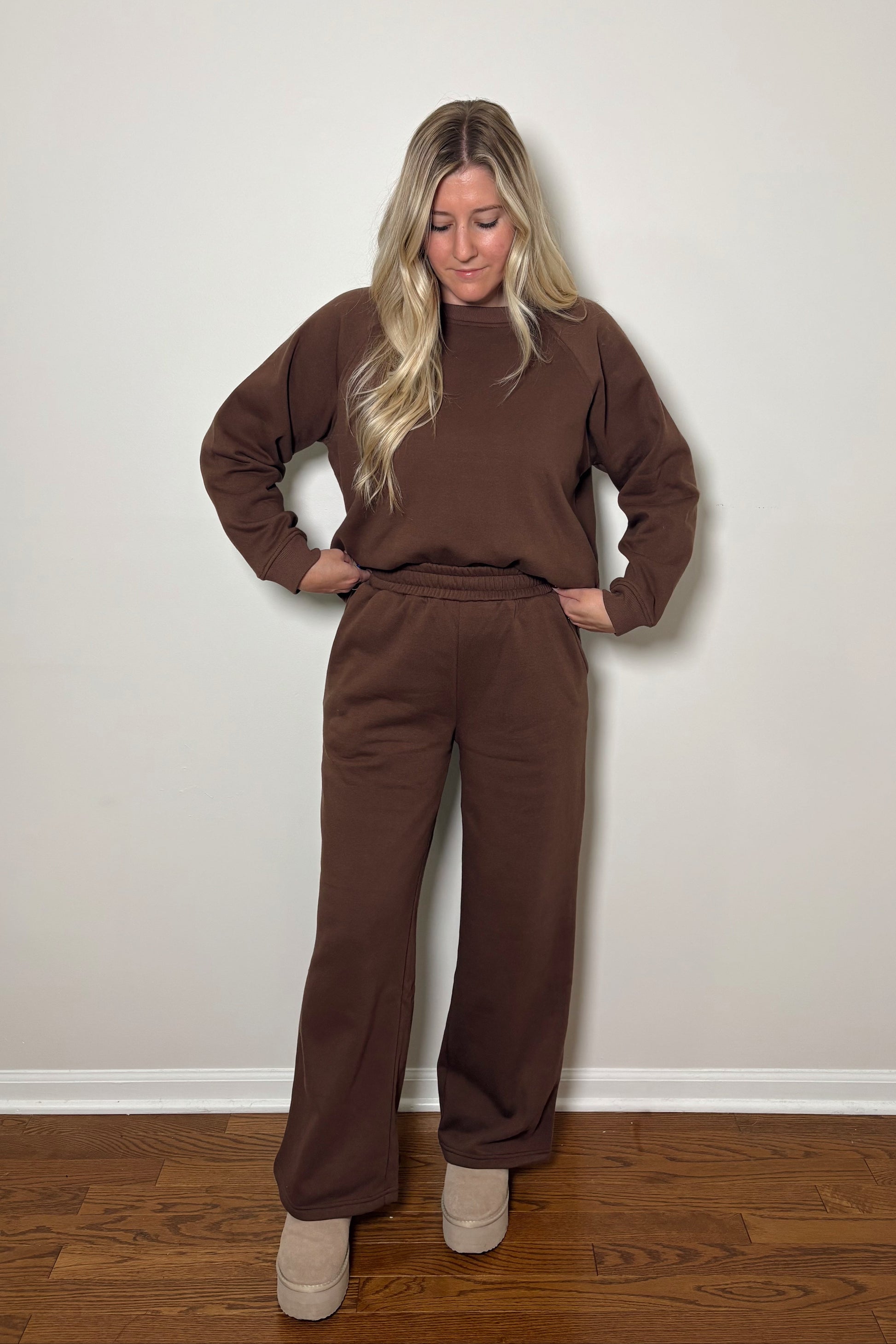 Woman wearing a brown sweat set/lounge set standing against a plain wall.