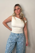 Clean Slate white asymmetrical top with a twisted shoulder detail and ruched waist, styled with light-blue polka dot jeans.

