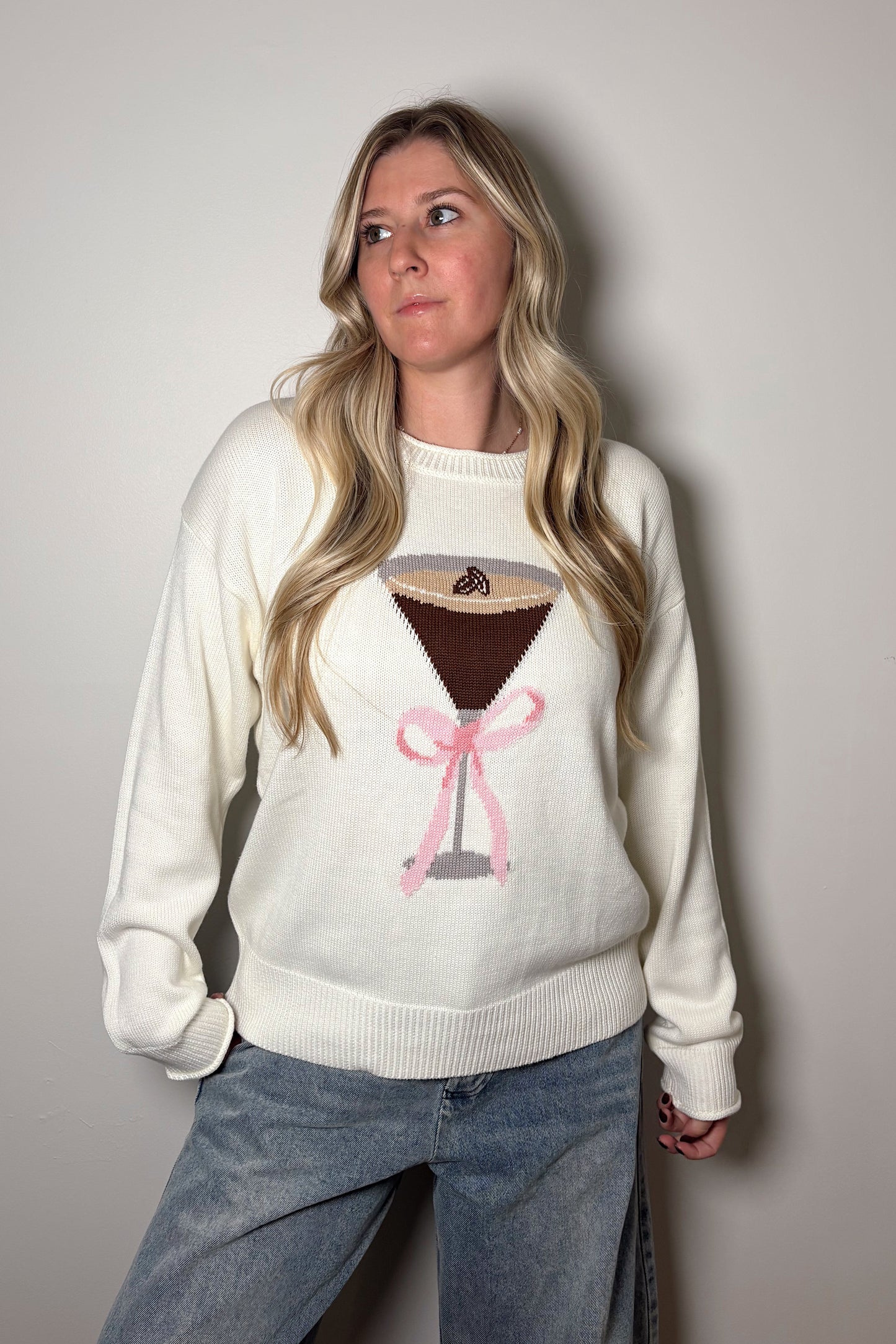 Person wearing a white sweater with a graphic design on a plain background