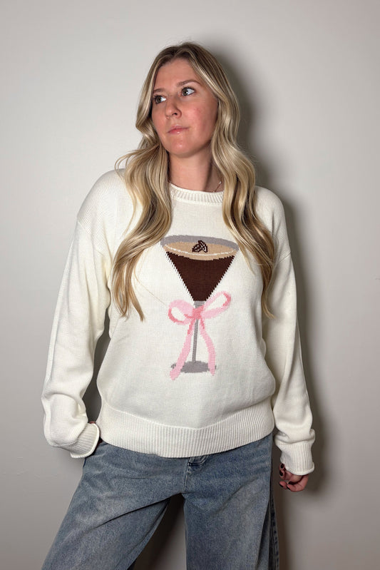 Person wearing a white sweater with a graphic design on a plain background