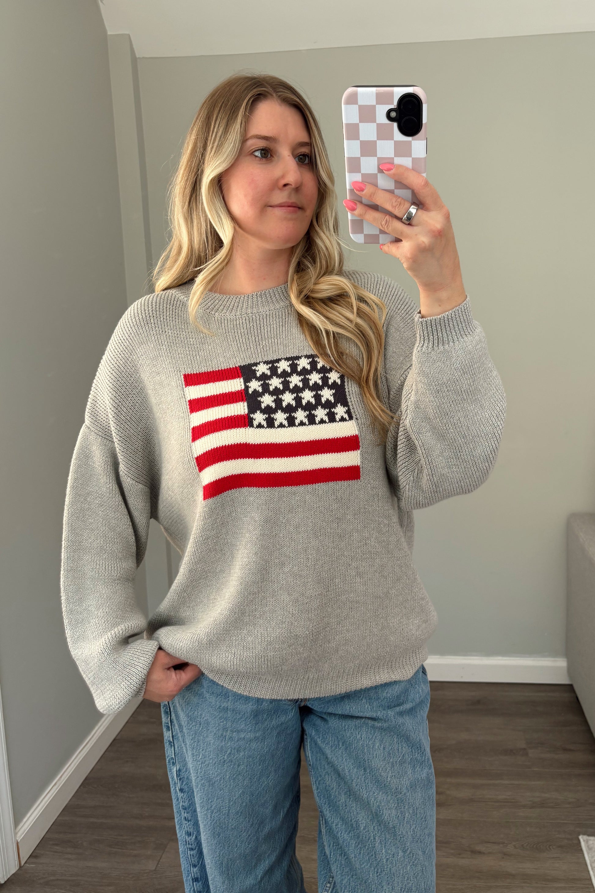 Person wearing a gray sweater with an American flag design, taking a mirror selfie.