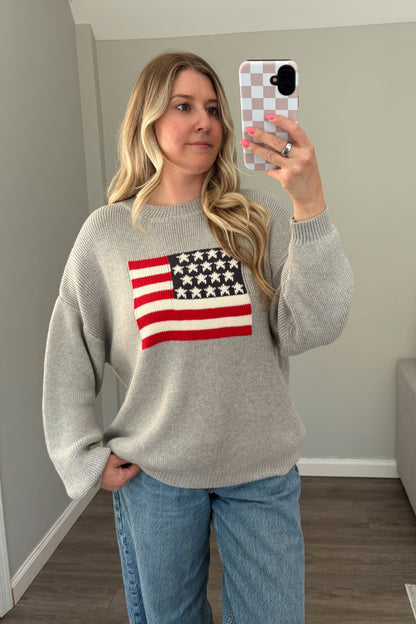 Person wearing a gray sweater with an American flag design, taking a mirror selfie.