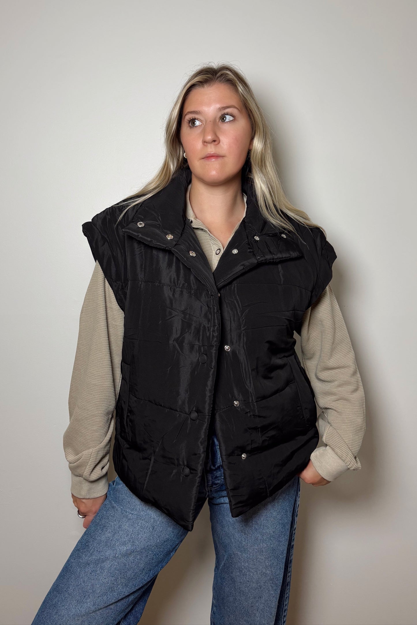Person wearing a black vest over a beige shirt with a plain background