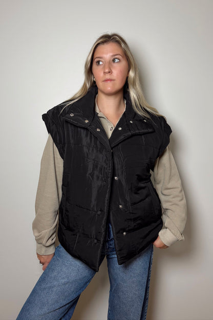 Person wearing a black vest over a beige shirt with a plain background