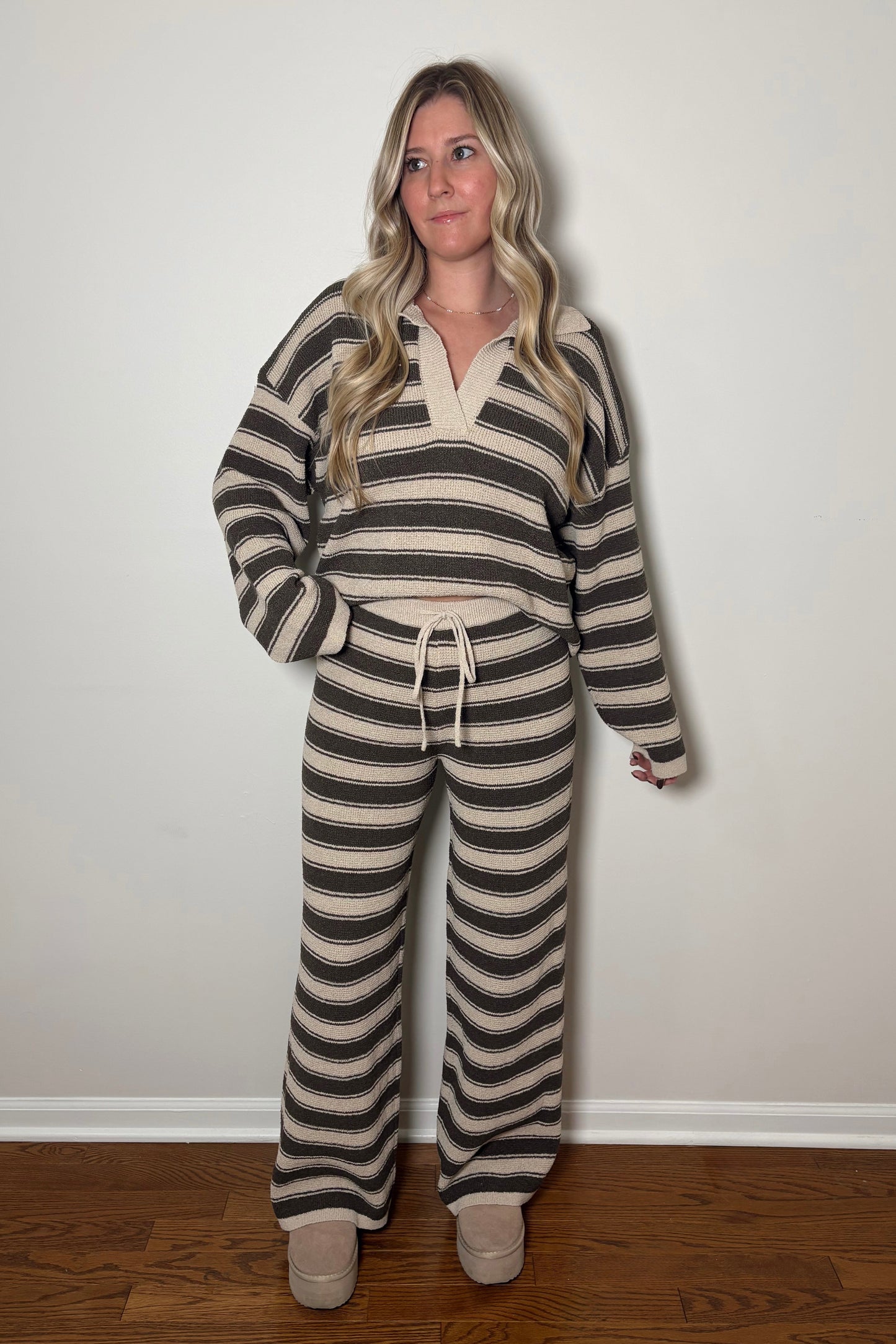 Woman wearing a striped outfit standing against a plain wall.