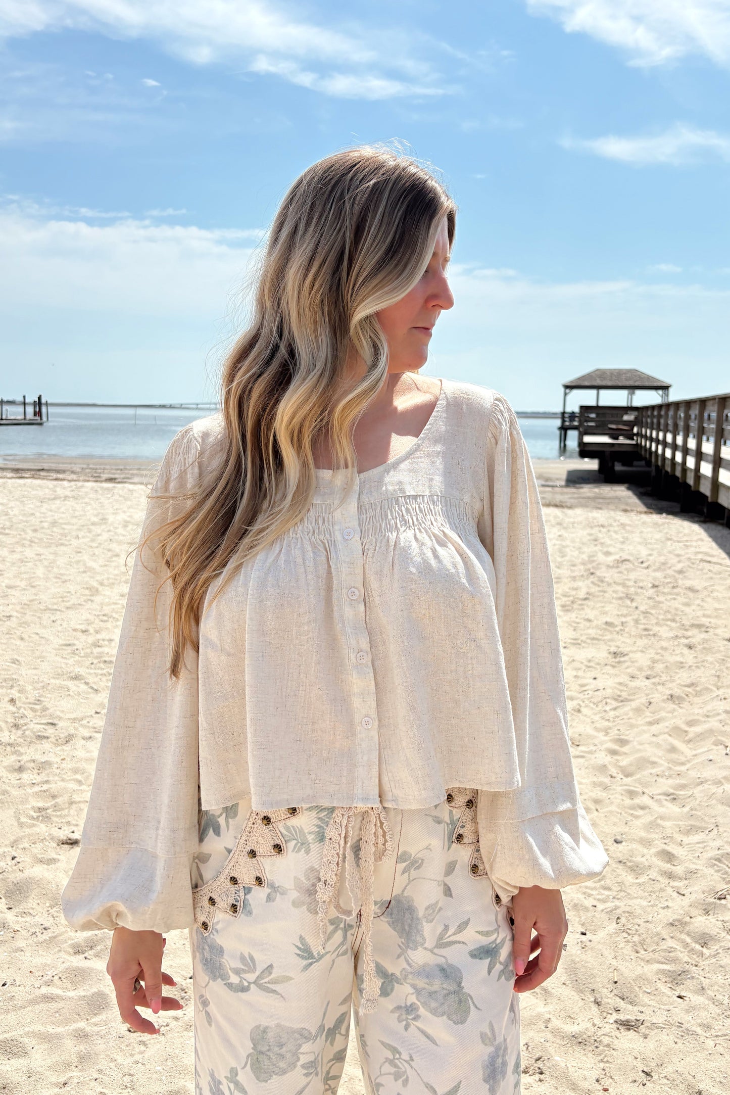 Person wearing a white shirt with floral patterned pants on a beach.