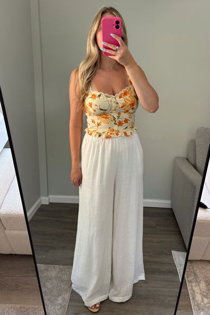 Woman taking a mirror selfie wearing a floral top and white pants.