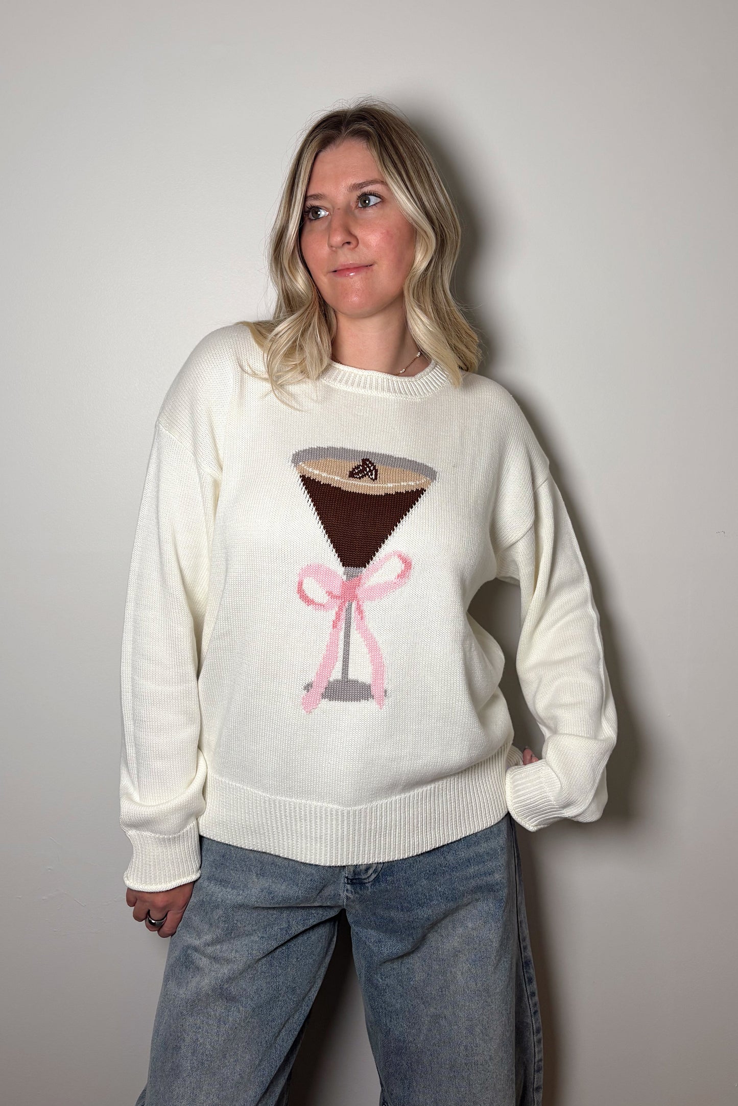 Person wearing a white sweater with a coffee-themed design against a plain background