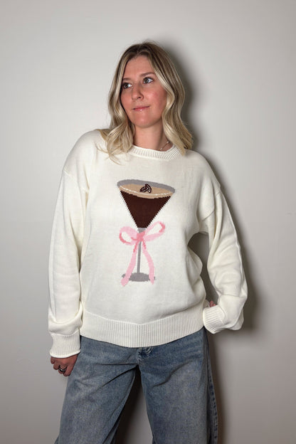 Person wearing a white sweater with a coffee-themed design against a plain background