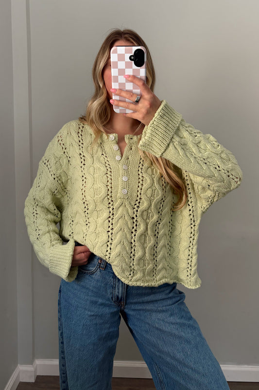 Person wearing a light green knitted sweater and blue jeans indoors.