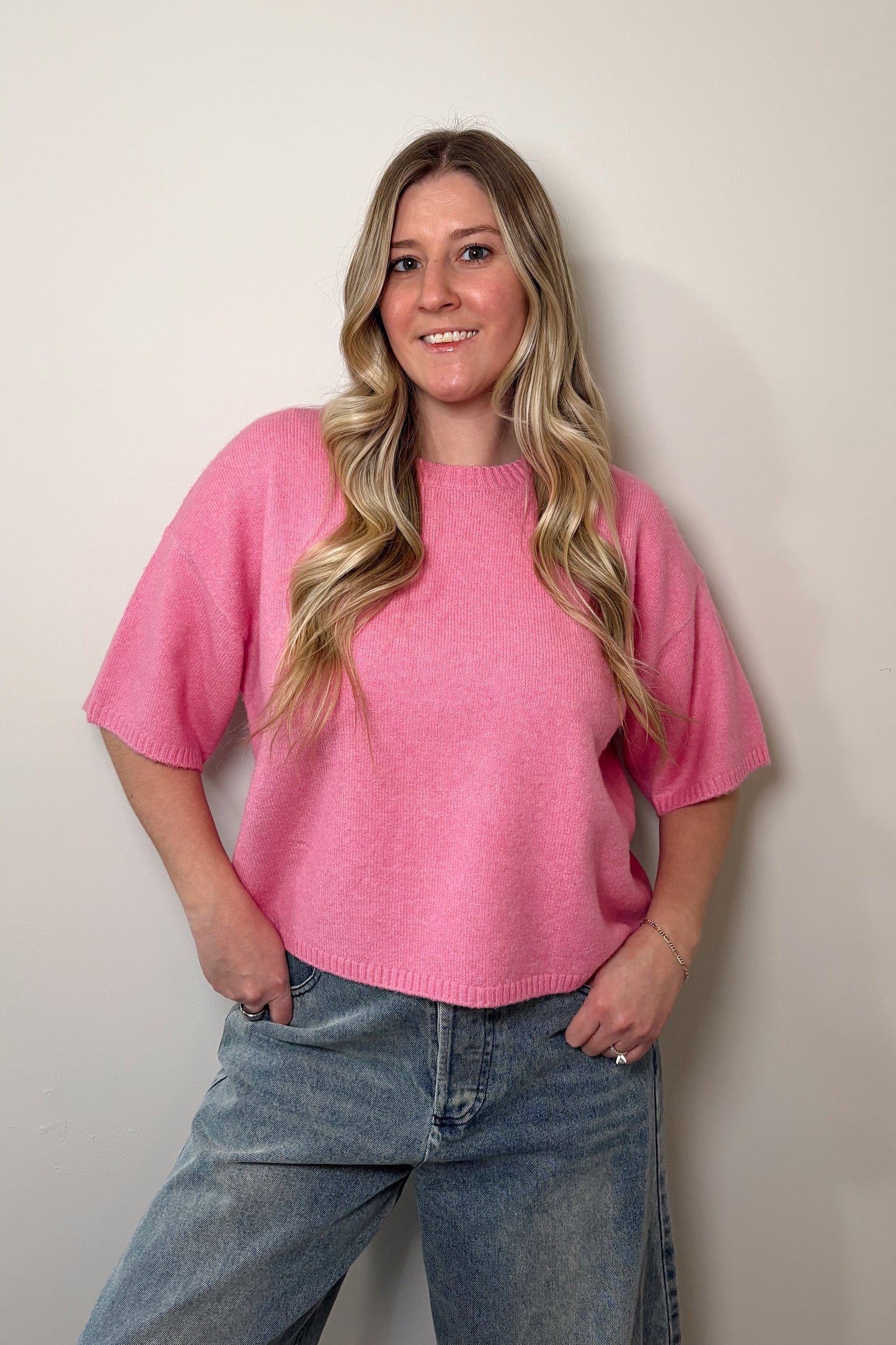 Person wearing a pink sweater and jeans against a plain background