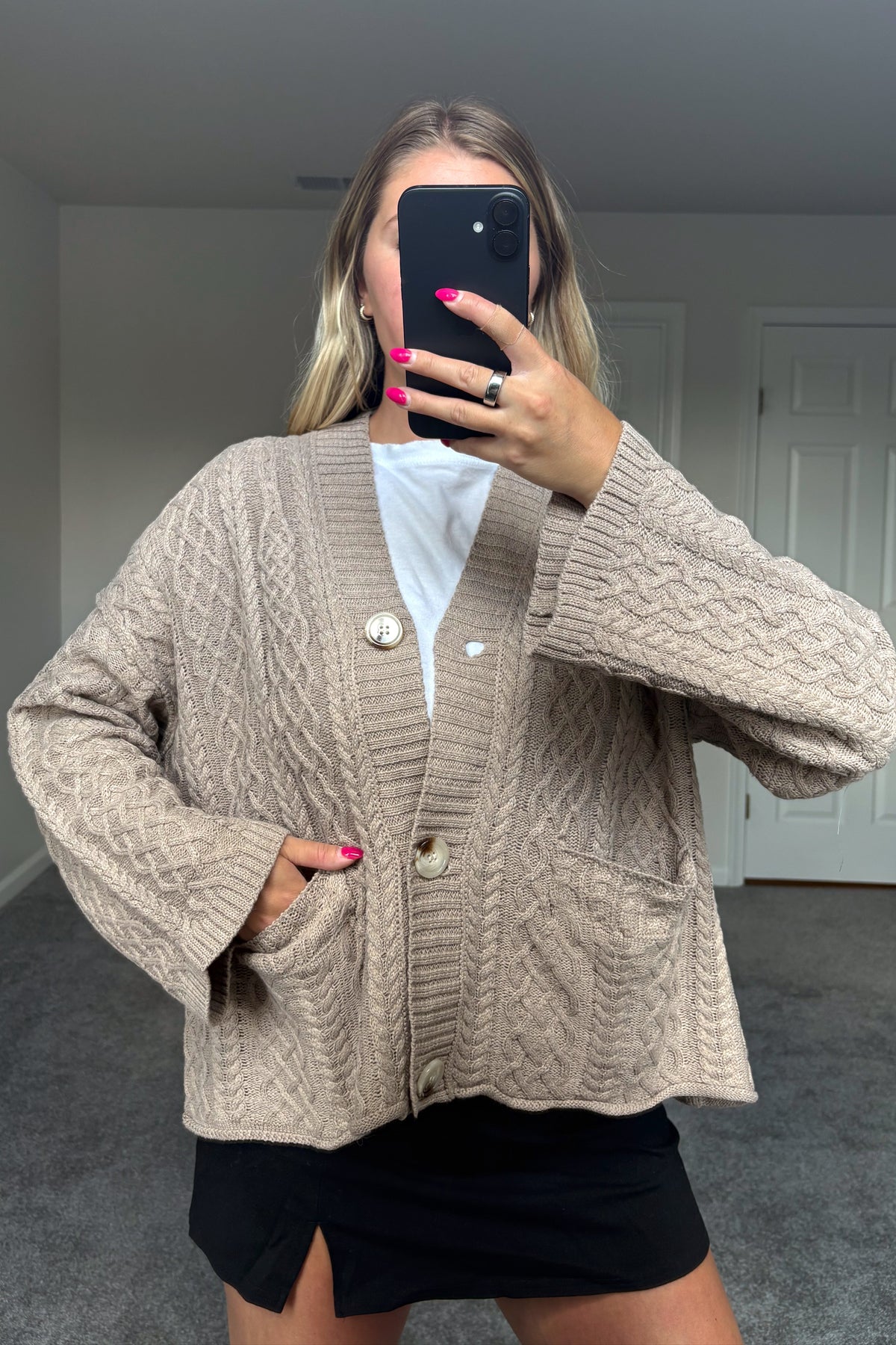 Fireside button-front cable knit cardigan worn with one hand in a front patch pocket, showing the ribbed trim and wide sleeve cuffs.

