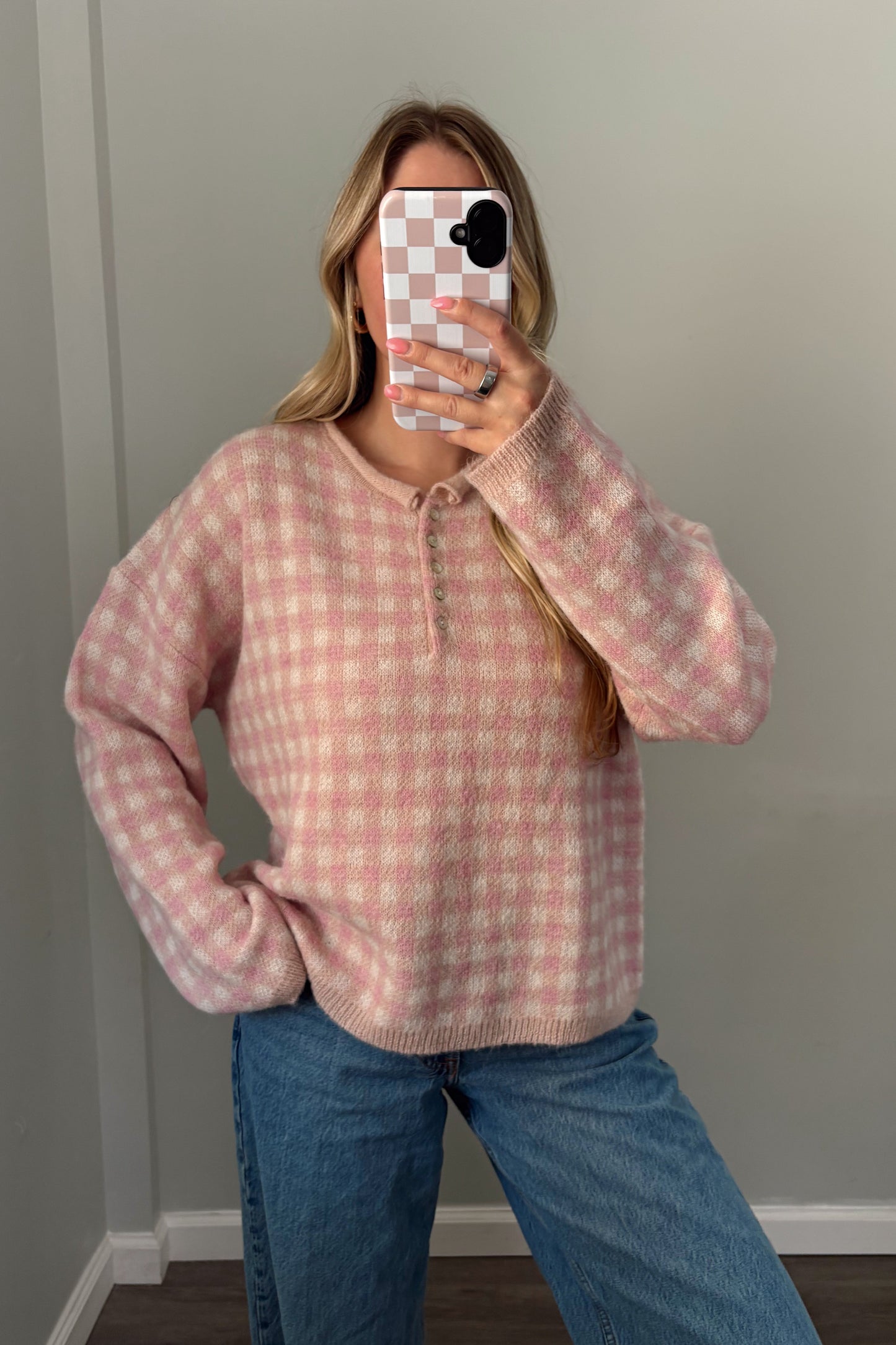 Person wearing a pink checkered shirt and blue jeans in a minimal indoor setting.