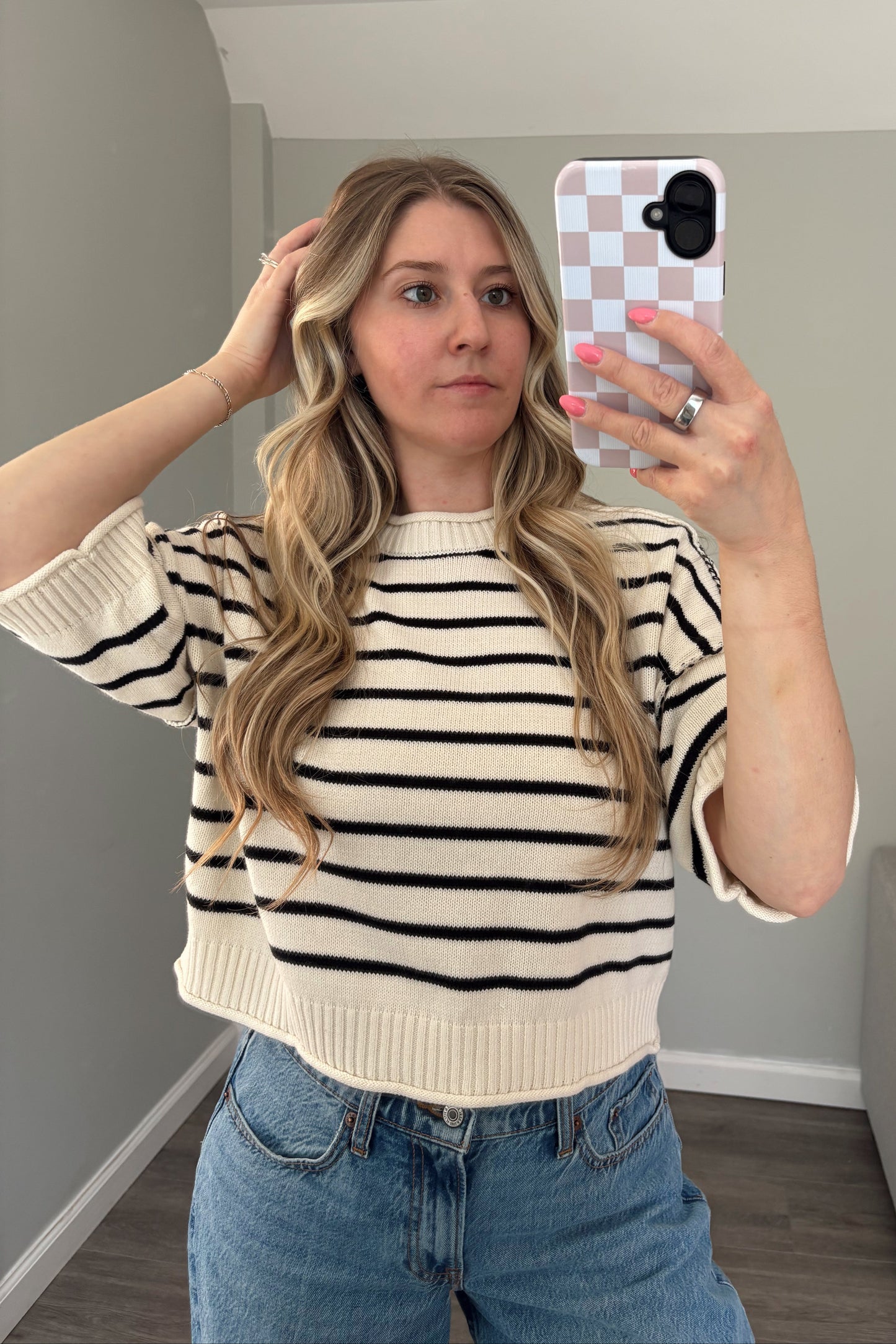 Person wearing a striped sweater and denim shorts taking a mirror selfie.