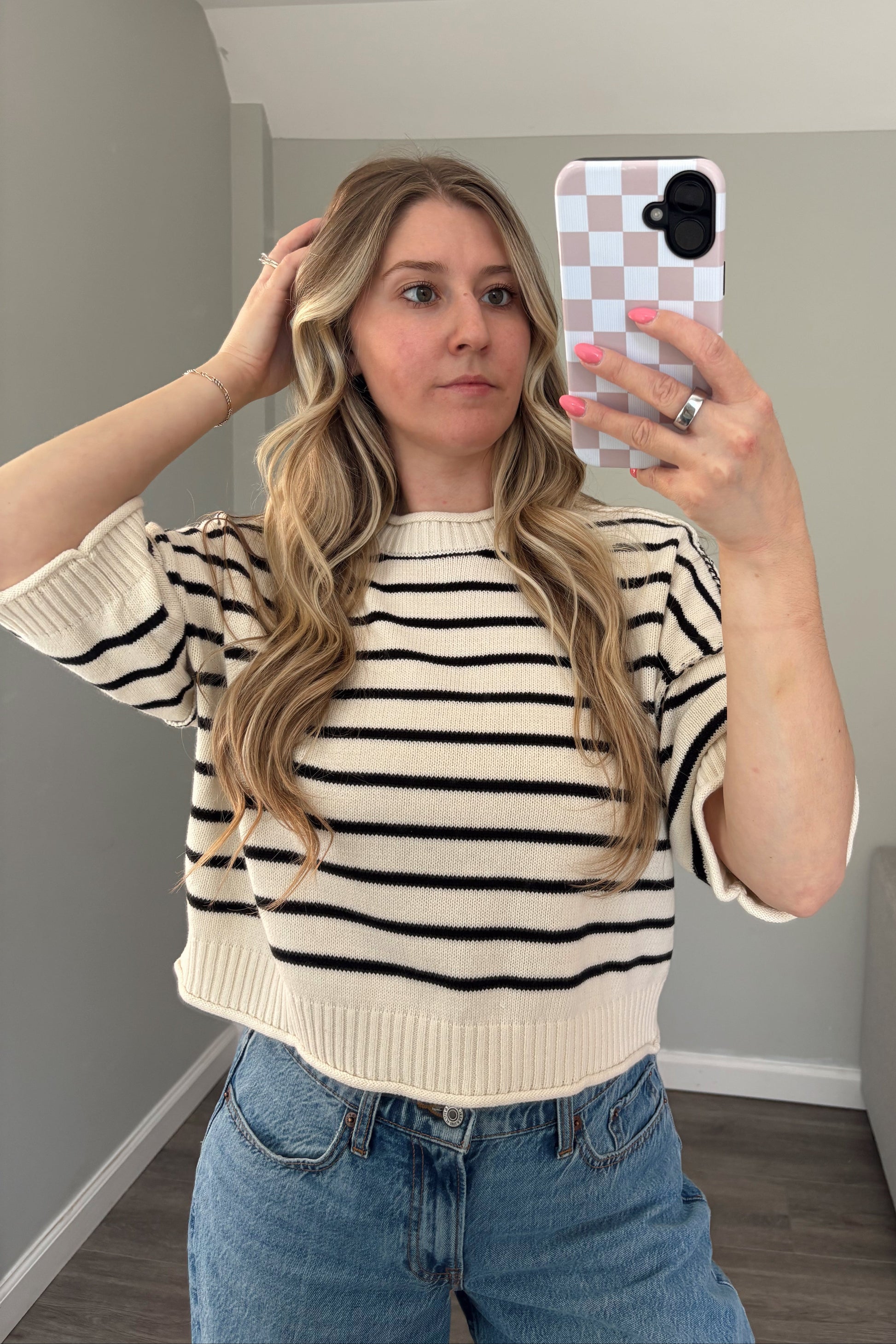 Person wearing a striped sweater and denim shorts taking a mirror selfie.