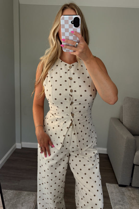 A woman takes a mirror selfie wearing a cream-colored sleeveless top with brown polka dots. The top features a button-up front, a fitted waist, and she is wearing matching wide-leg pants.
