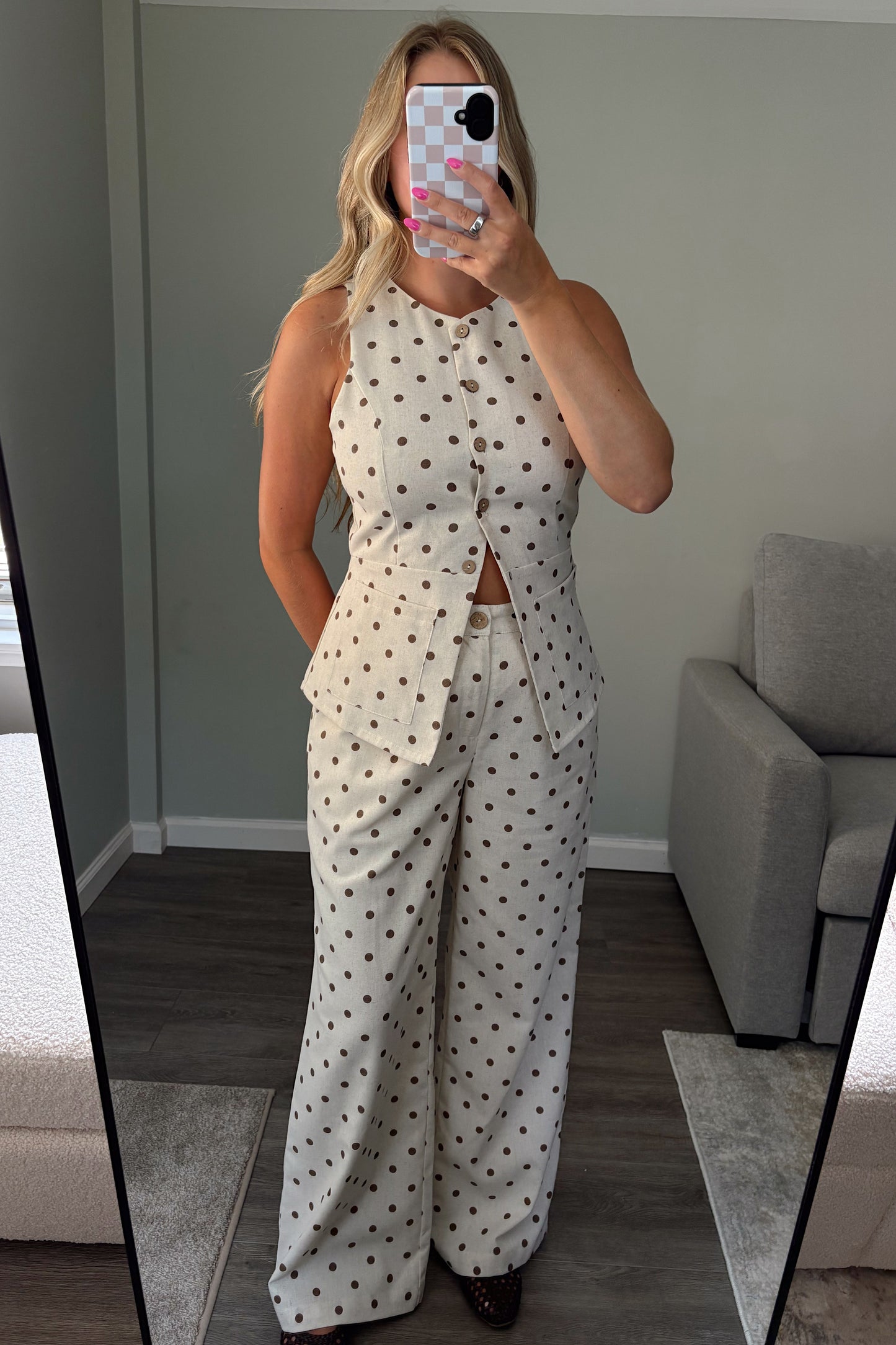 A woman takes a mirror selfie in a room wearing a matching two-piece set consisting of a sleeveless button-front top and wide-leg trousers, both in an off-white fabric with small dark polka dots.