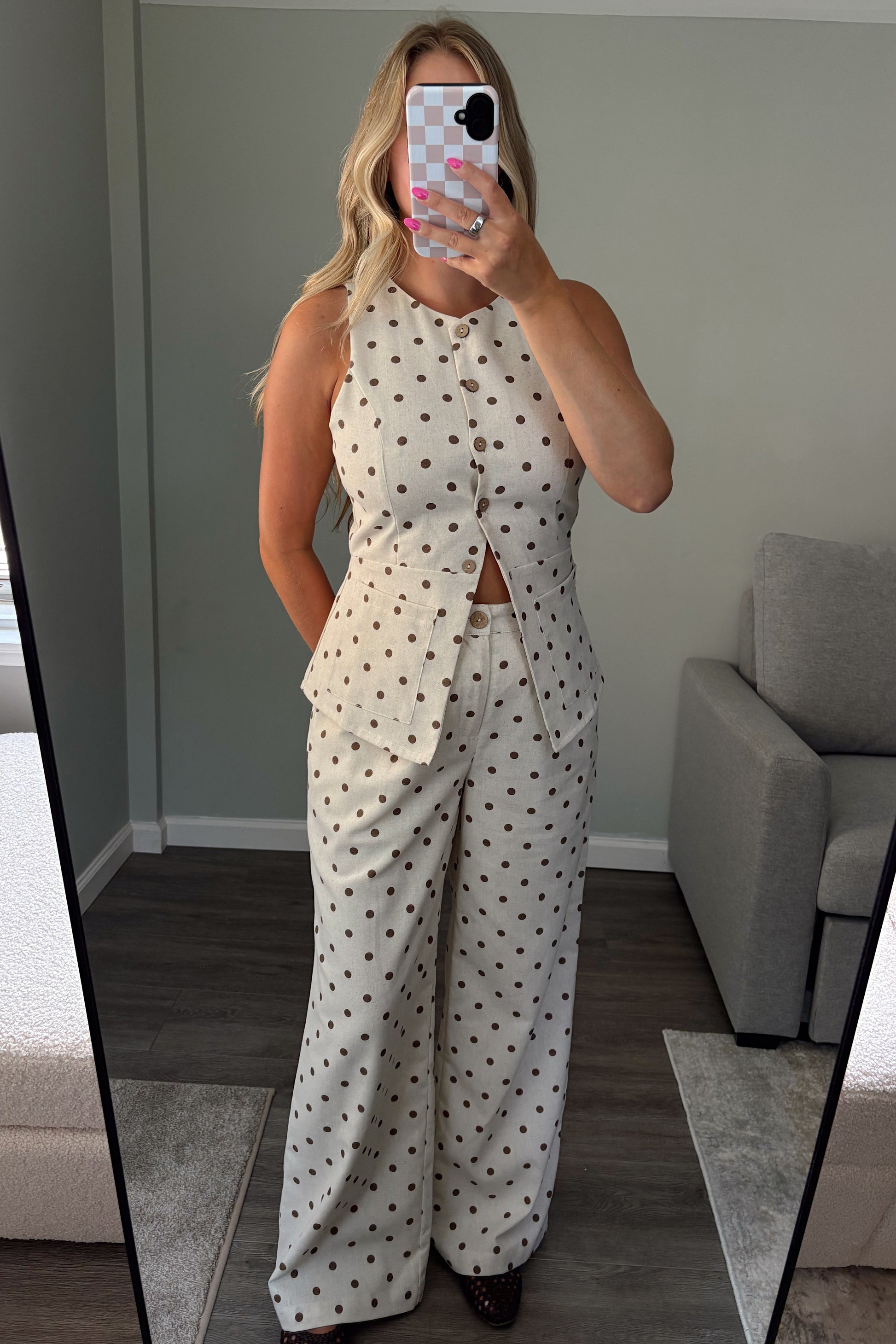 A woman takes a mirror selfie in a room wearing a matching two-piece set consisting of a sleeveless button-front top and wide-leg trousers, both in an off-white fabric with small dark polka dots.
