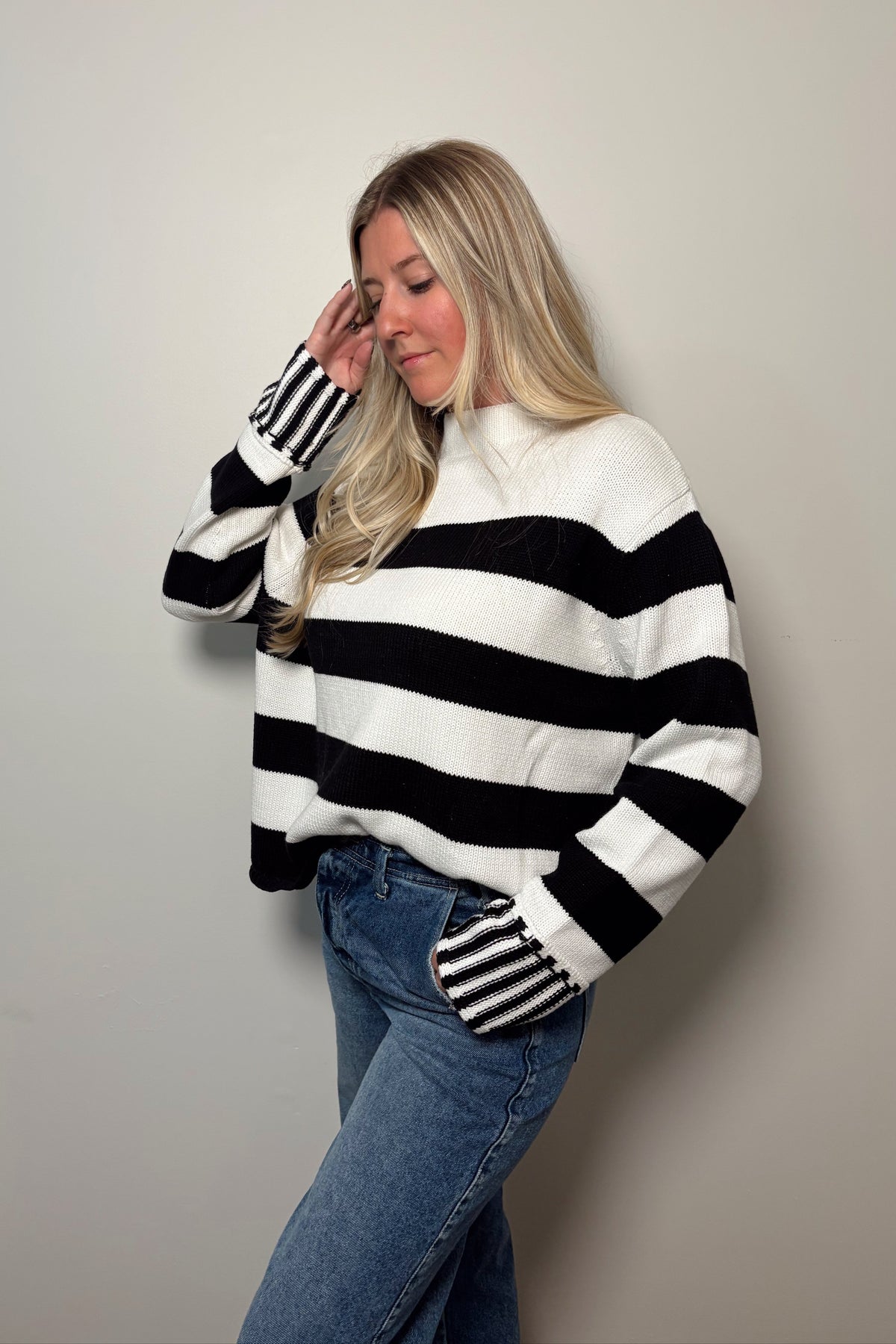 Angled front view of the Sunday Brunch sweater with one hand raised, highlighting the contrasting vertical stripes on the cuffs.

