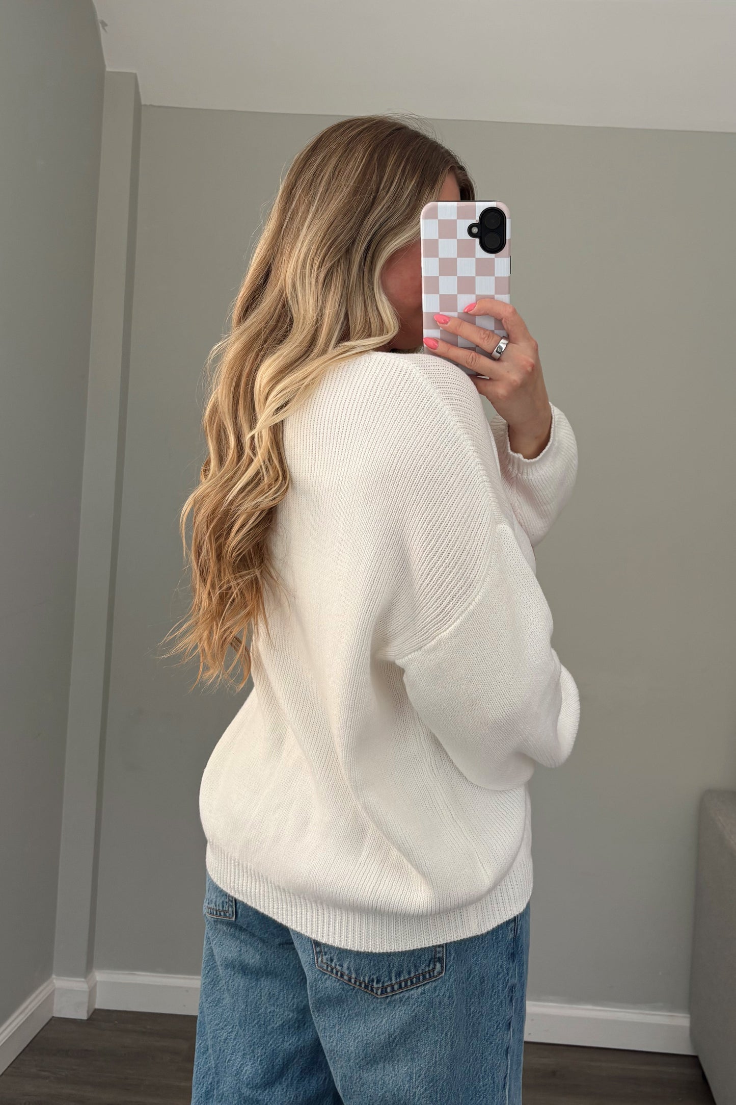 Person wearing a white sweater and blue jeans standing in front of a mirror.