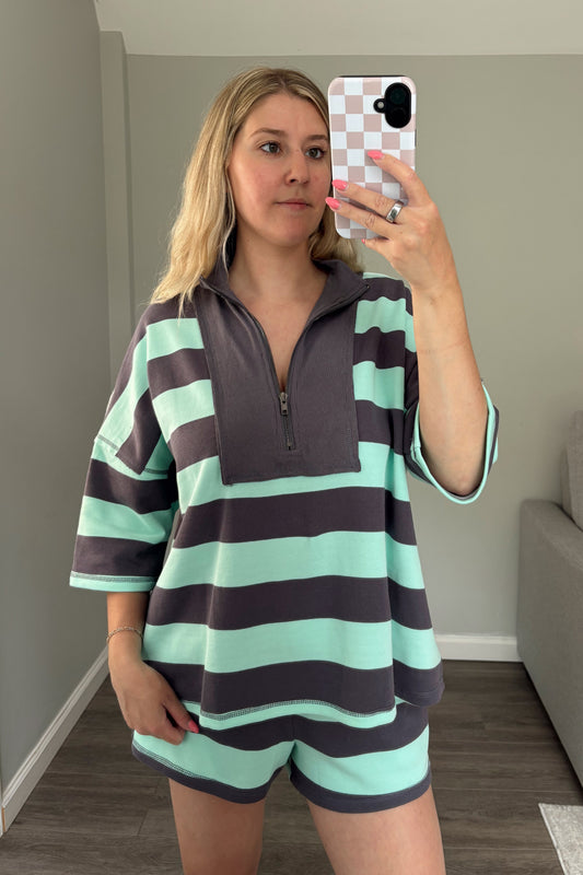 Person wearing a striped shirt and shorts taking a mirror selfie in a room.