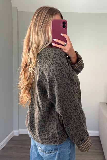 A woman takes a mirror selfie in a room, wearing an oversized dark olive green and brown leopard print cardigan with blue jeans.