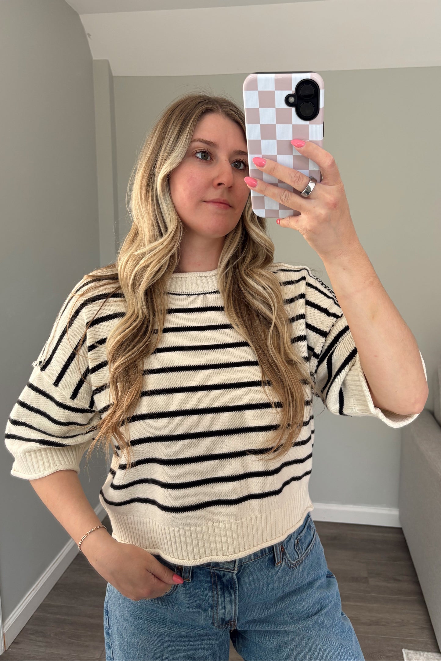 Woman taking a mirror selfie wearing a striped sweater and jeans in a living room.