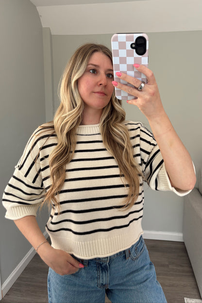 Woman taking a mirror selfie wearing a striped sweater and jeans in a living room.