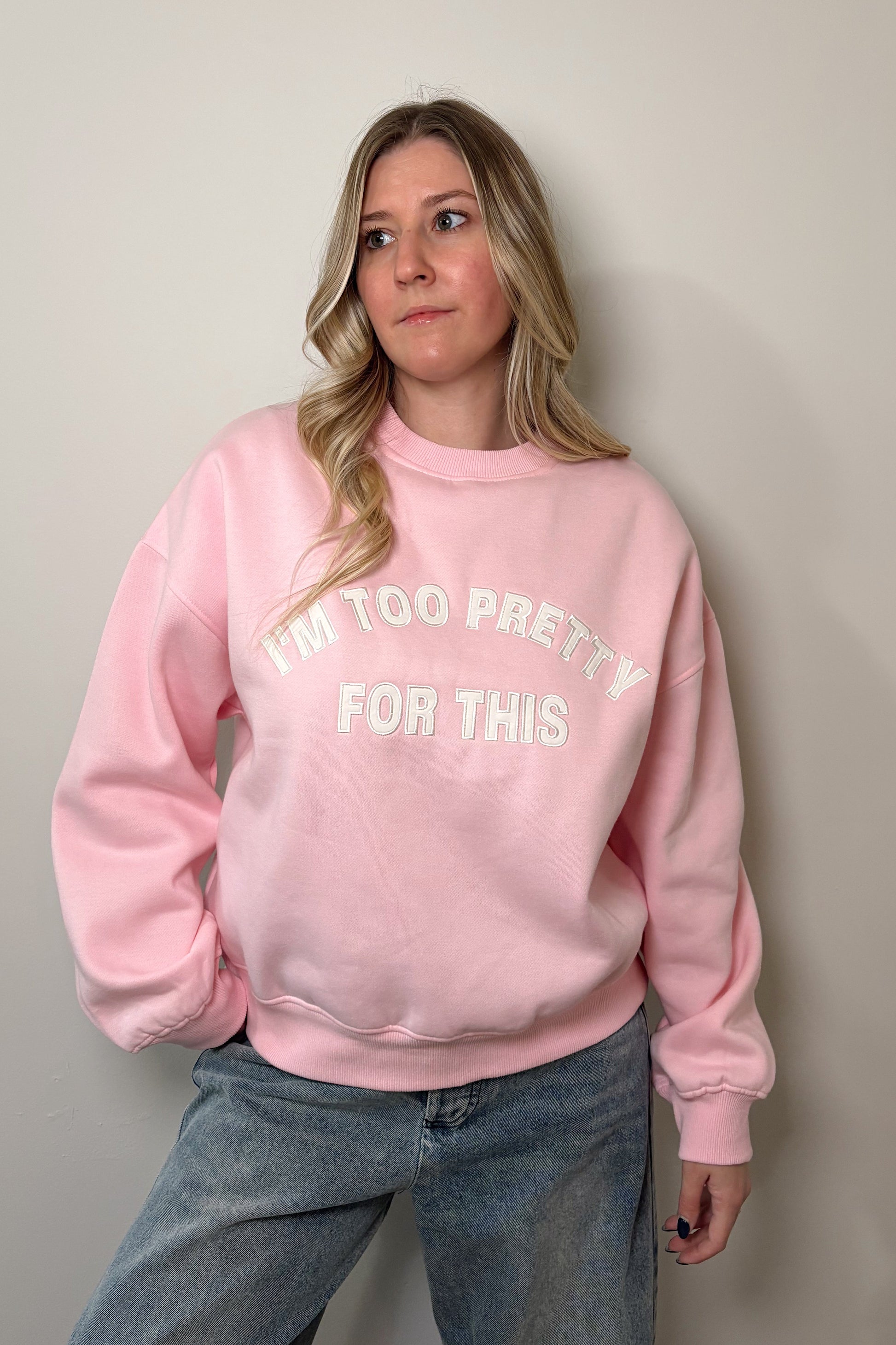 Person wearing a pink sweatshirt with "I'm too pretty for this" text, standing against a plain background