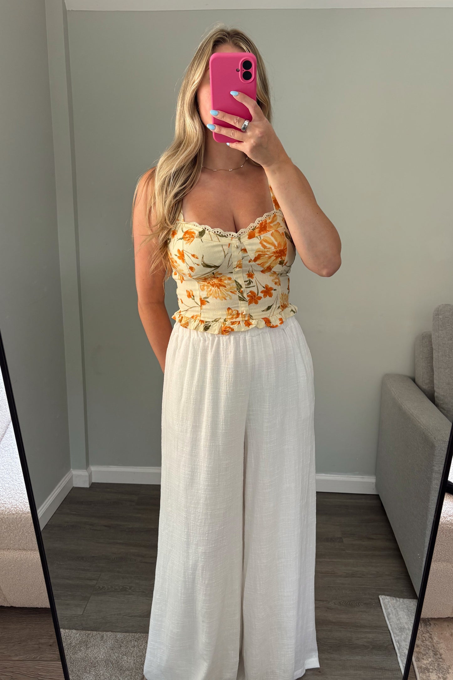 Woman taking a mirror selfie wearing a floral top and white pants.