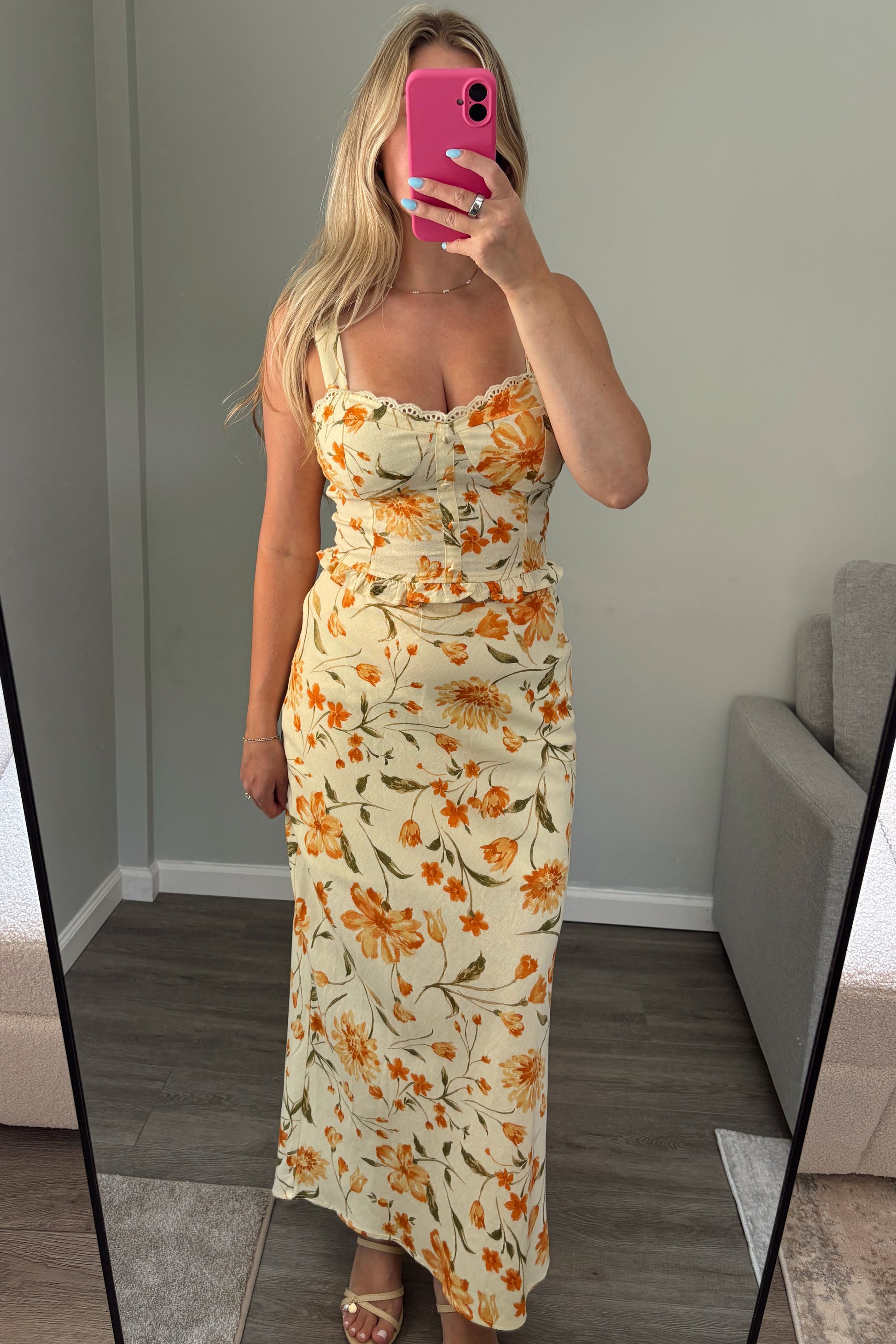 Woman in a floral top and skirt taking a mirror selfie in a modern interior setting.