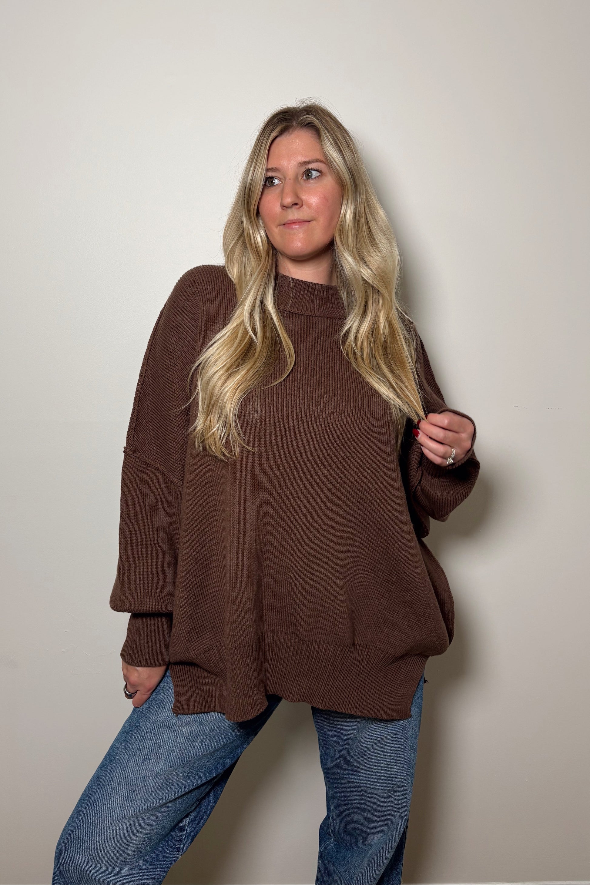 Woman wearing a brown sweater and blue jeans against a plain background