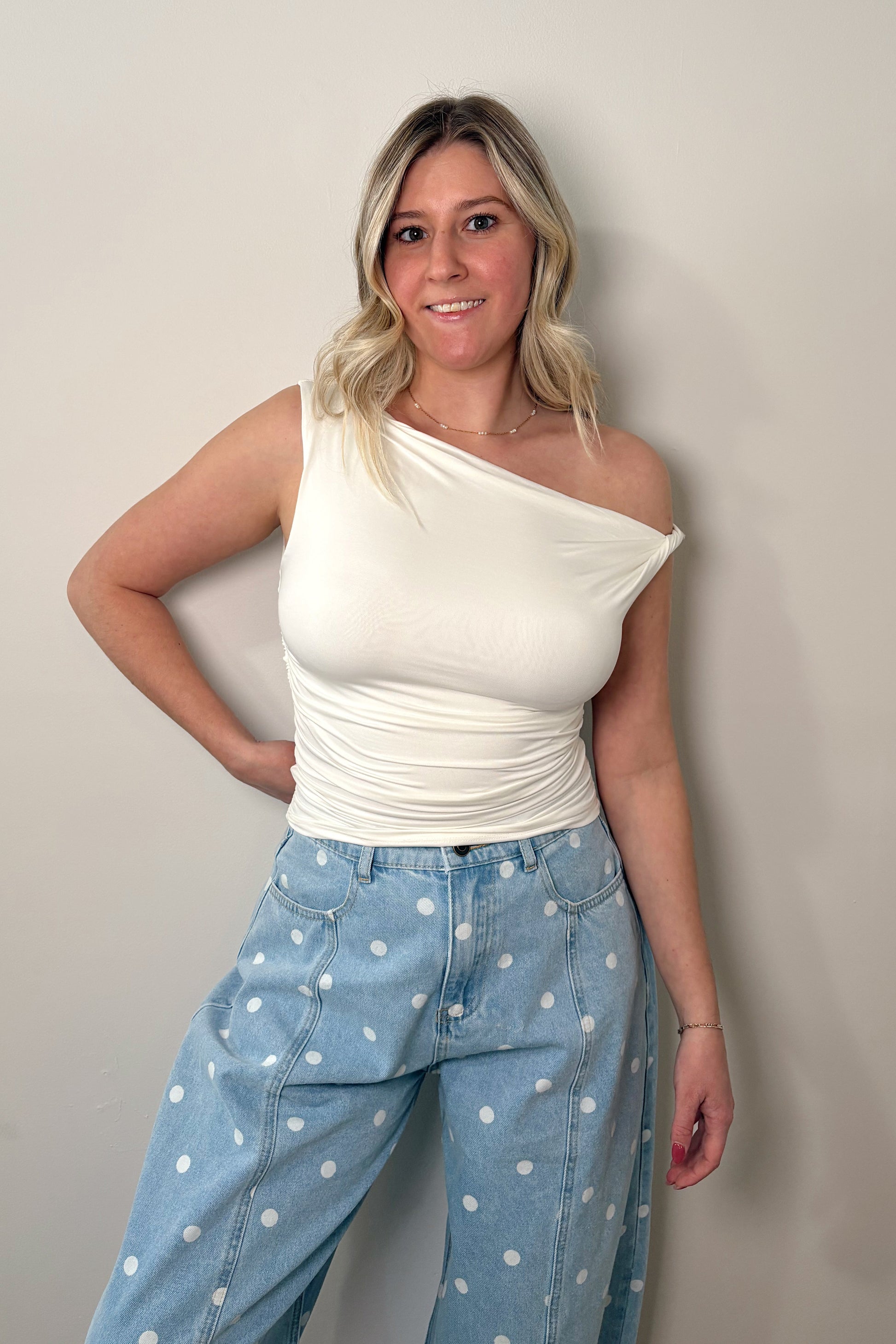 Woman wearing a white one-shoulder top and blue polka dot pants against a plain background
