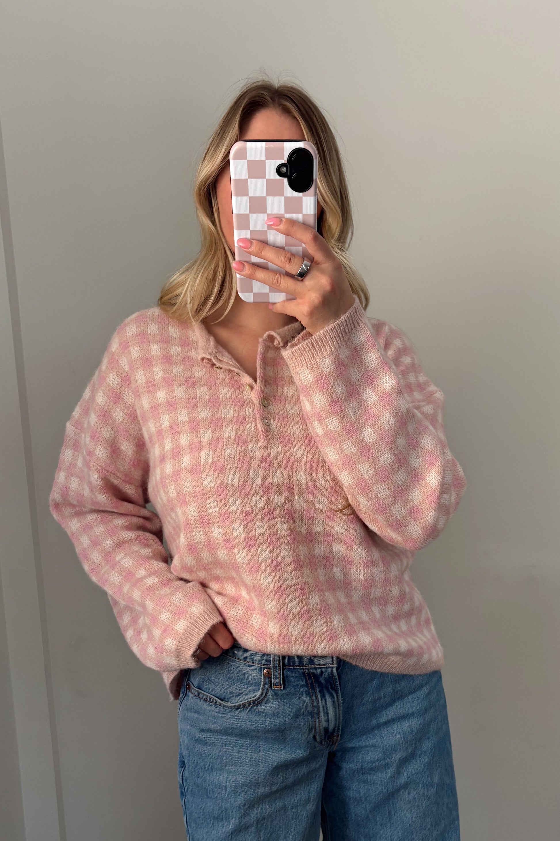 Person wearing a pink checkered hoodie and blue jeans standing in front of a mirror.