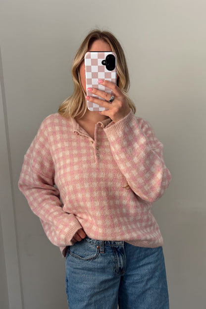 Person wearing a pink checkered hoodie and blue jeans standing in front of a mirror.