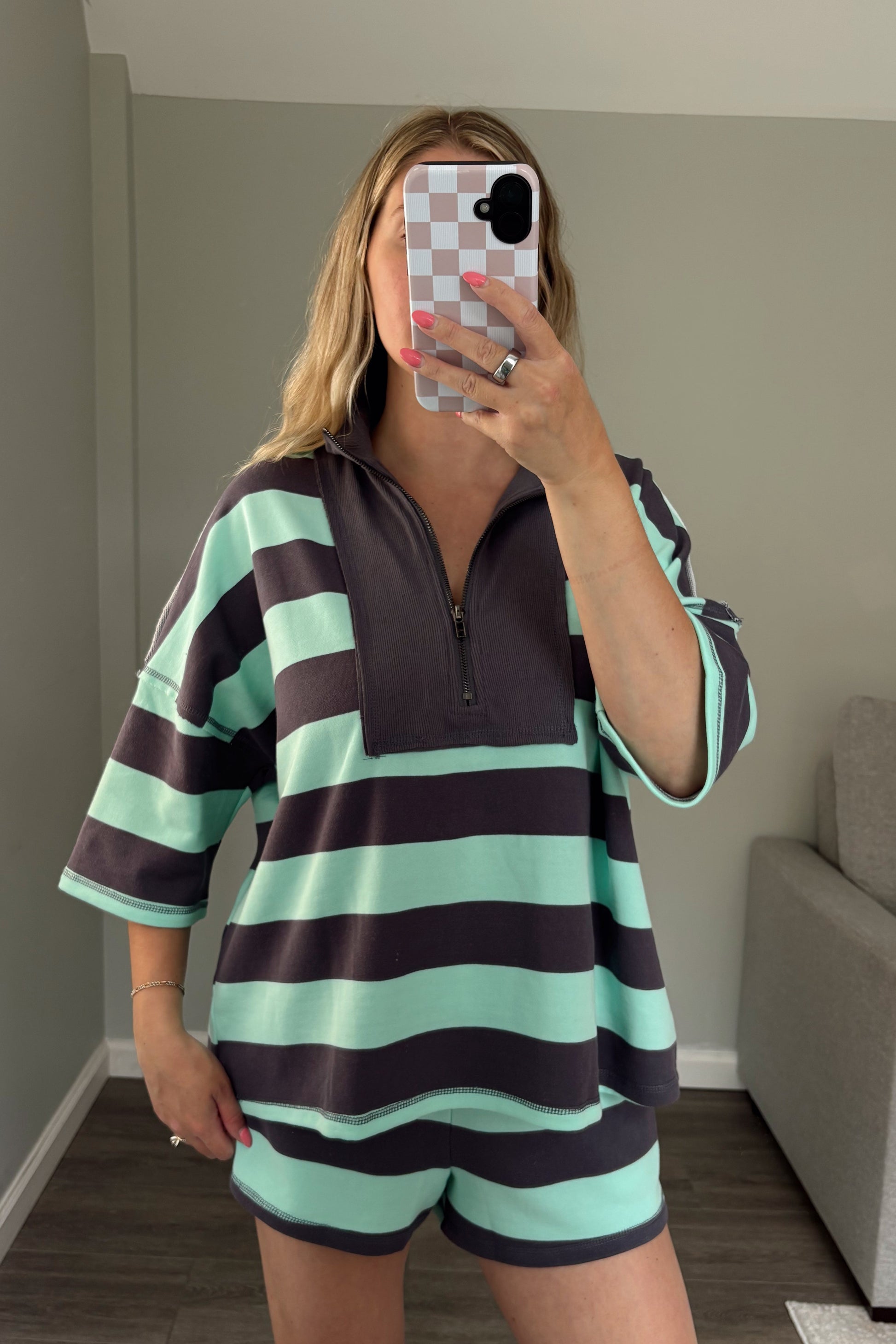 Person wearing a striped outfit taking a mirror selfie in a room with a couch.