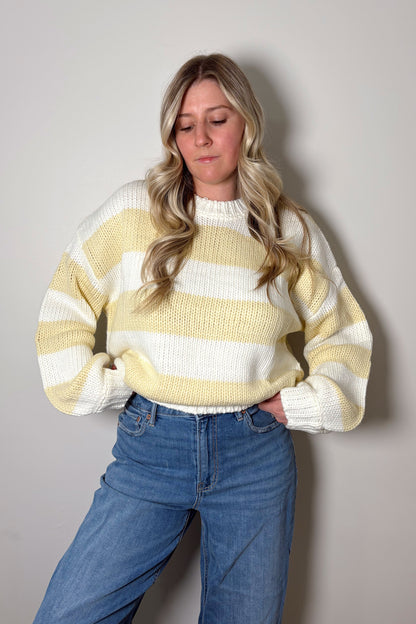 Person wearing a yellow and white striped sweater and blue jeans against a plain background