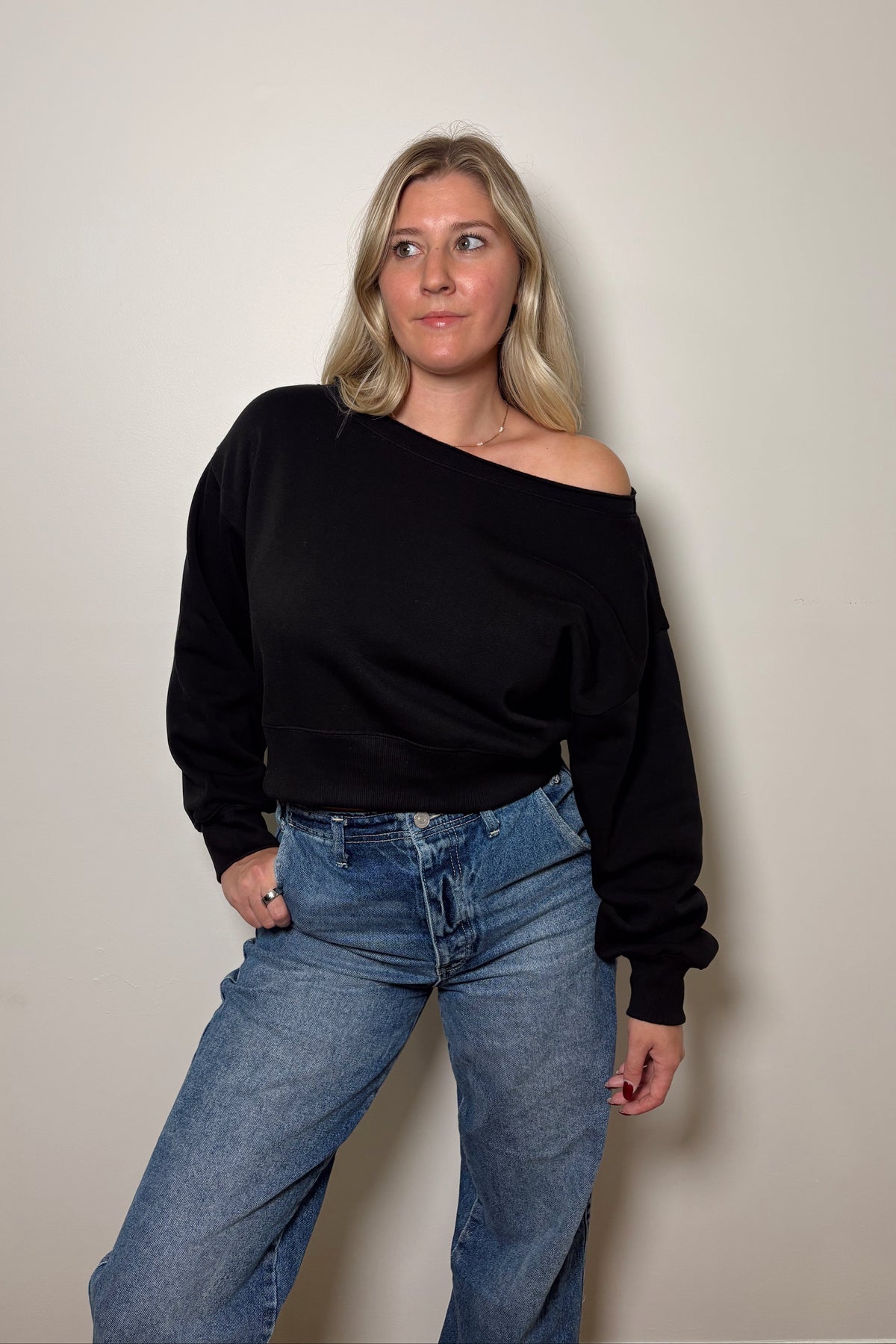 Front view of the Haven black fleece pullover worn off one shoulder with high-rise blue jeans.

