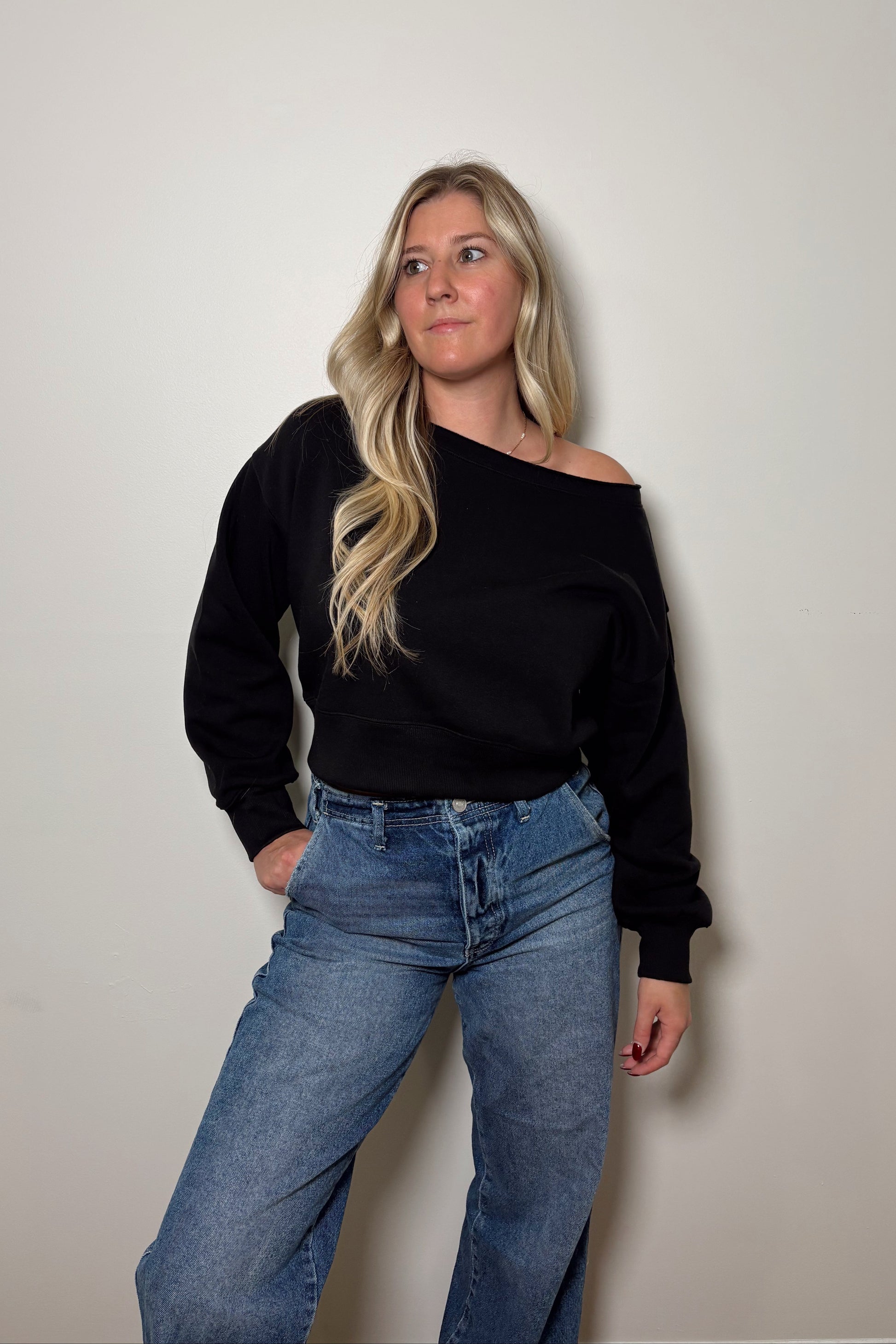 Person wearing a black off-shoulder top and blue jeans against a plain background