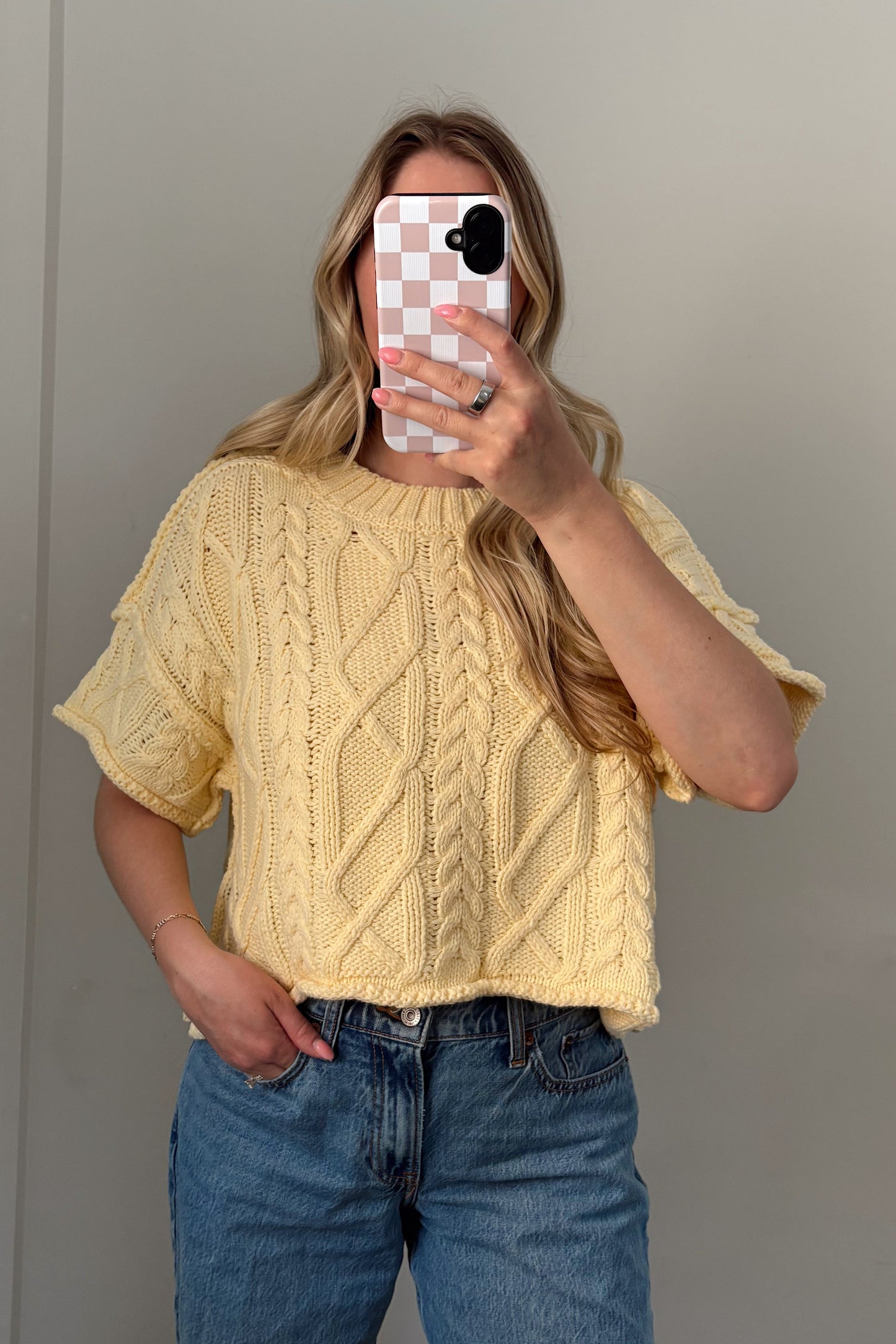 Person wearing a yellow sweater and blue jeans taking a mirror selfie.