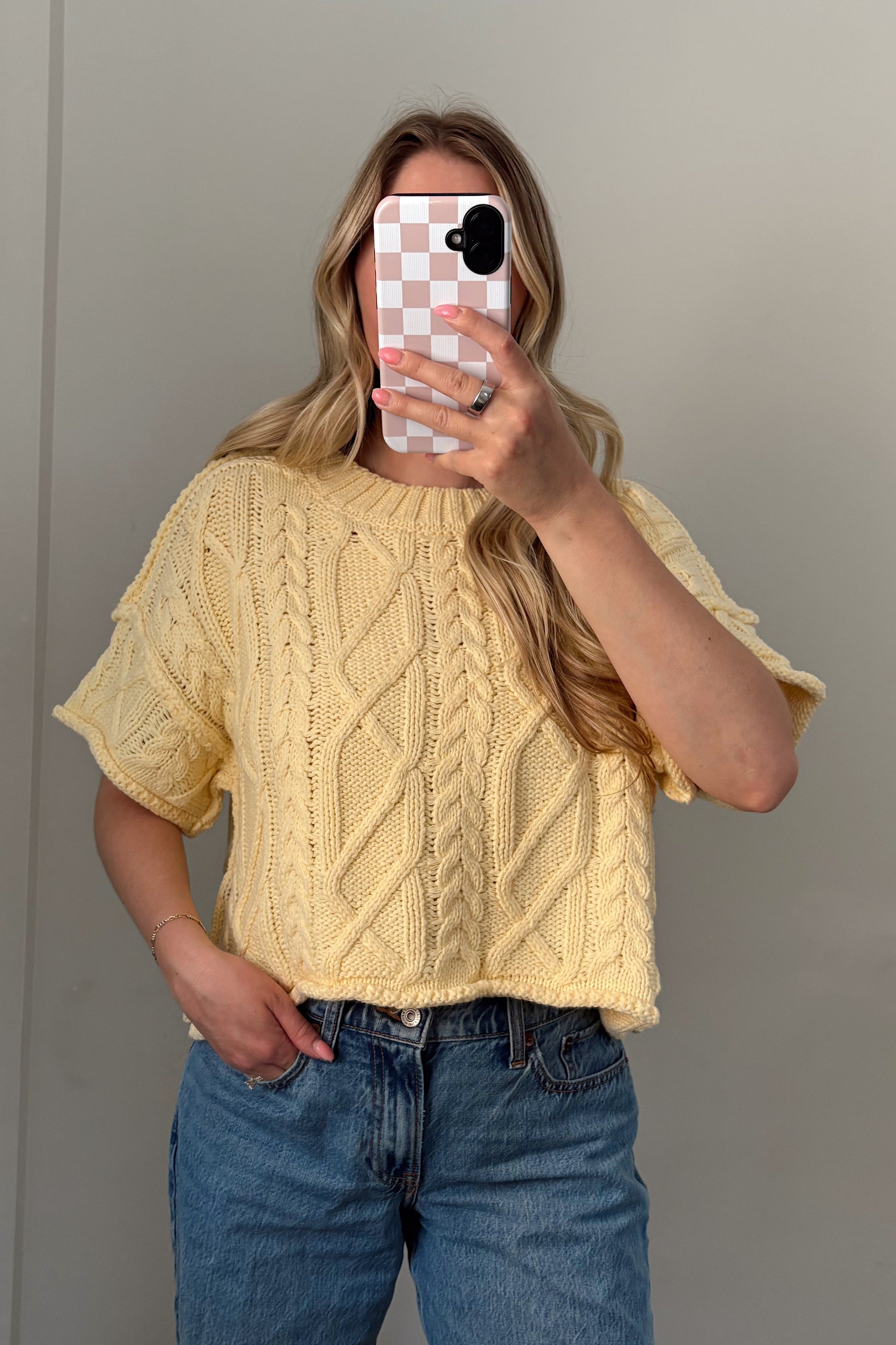 Person wearing a yellow sweater and blue jeans taking a mirror selfie.