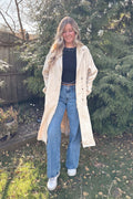 Woman wearing the beige Manhattan polka dot trench coat open over a black top and blue jeans outdoors