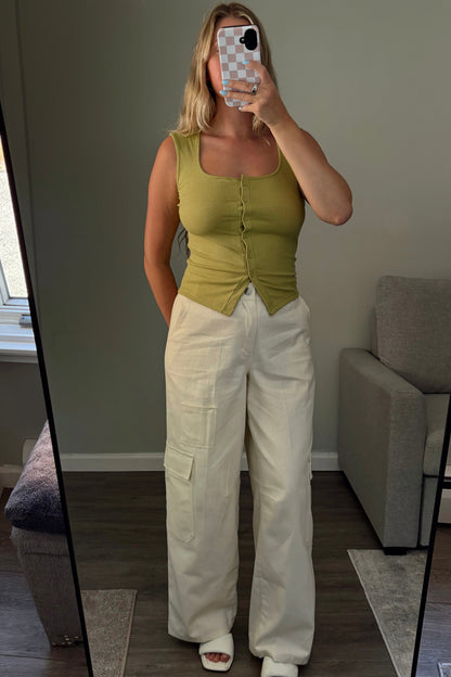 Person wearing a green tank top and white cargo pants taking a mirror selfie.