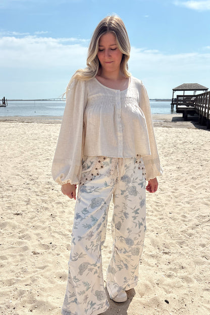 Person wearing a white shirt with floral patterned pants on a beach.