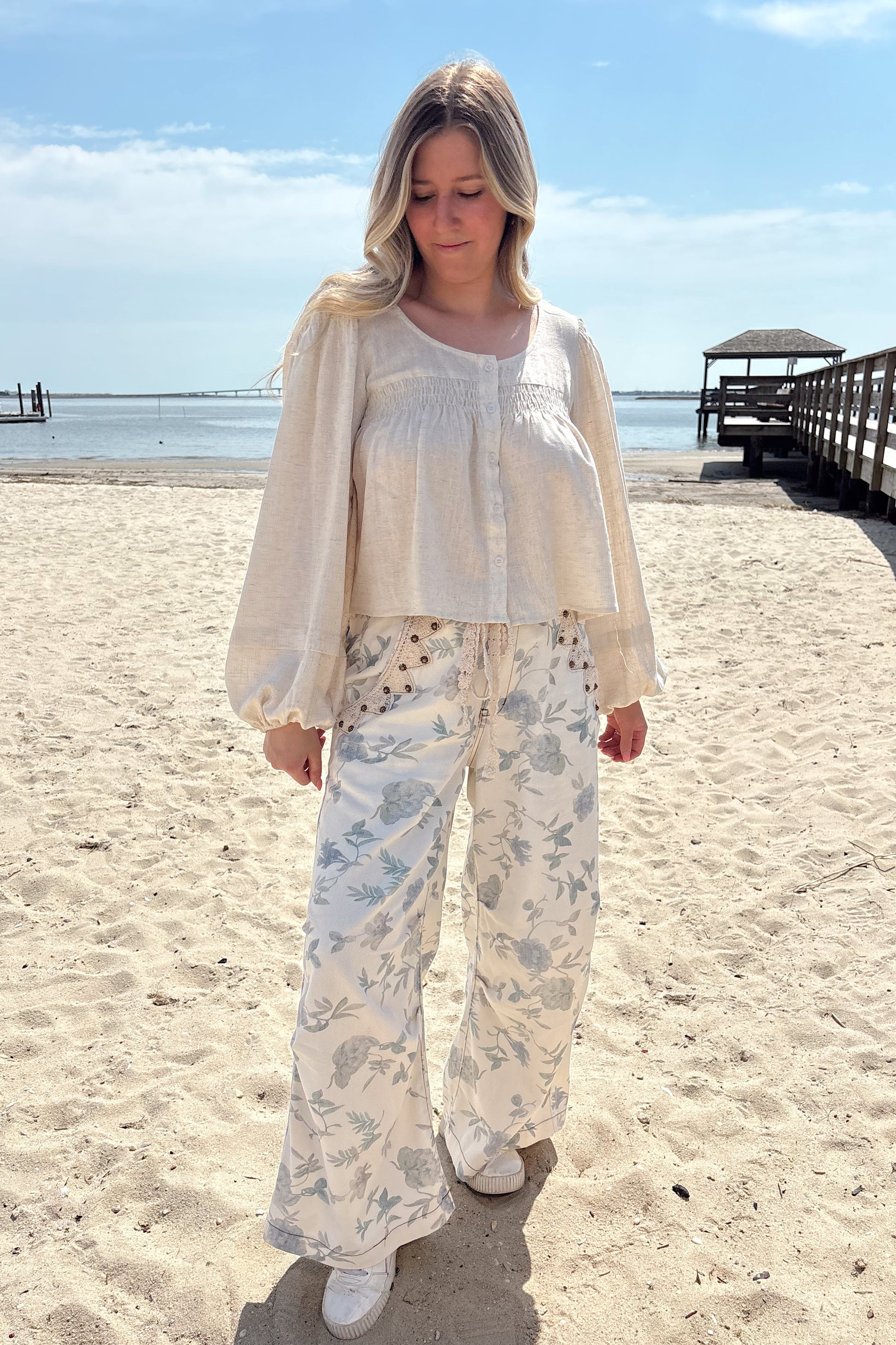 Person standing on a sandy beach wearing a light-colored outfit with floral patterns.
