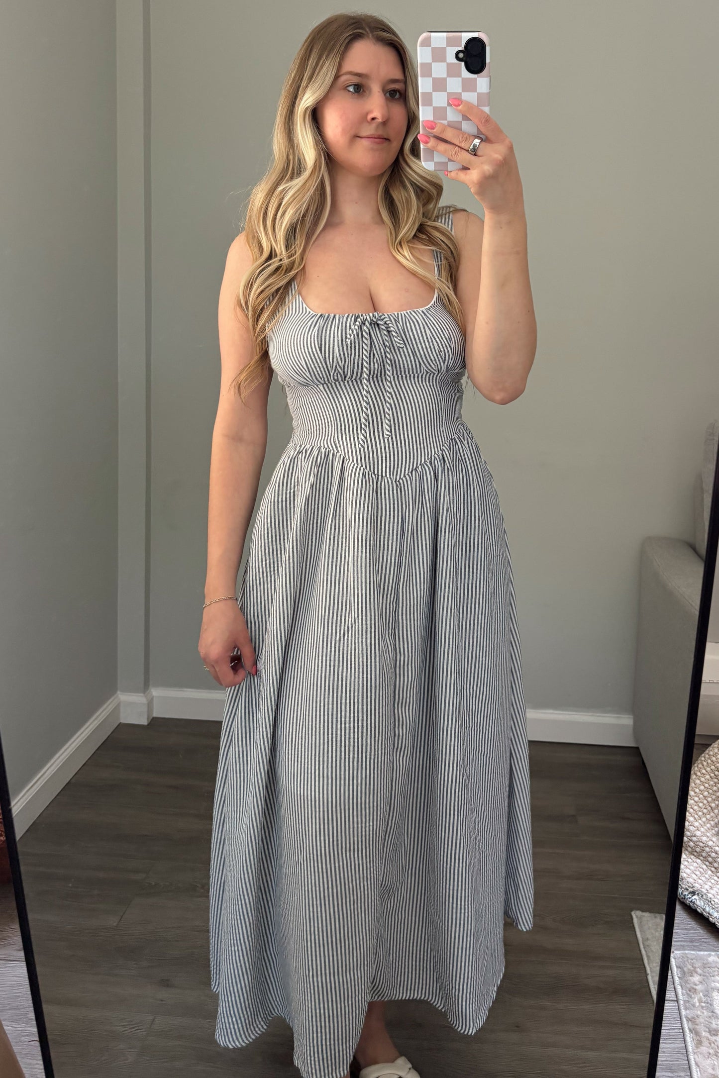 Woman taking a mirror selfie wearing a light blue dress in a room with a couch and window.
