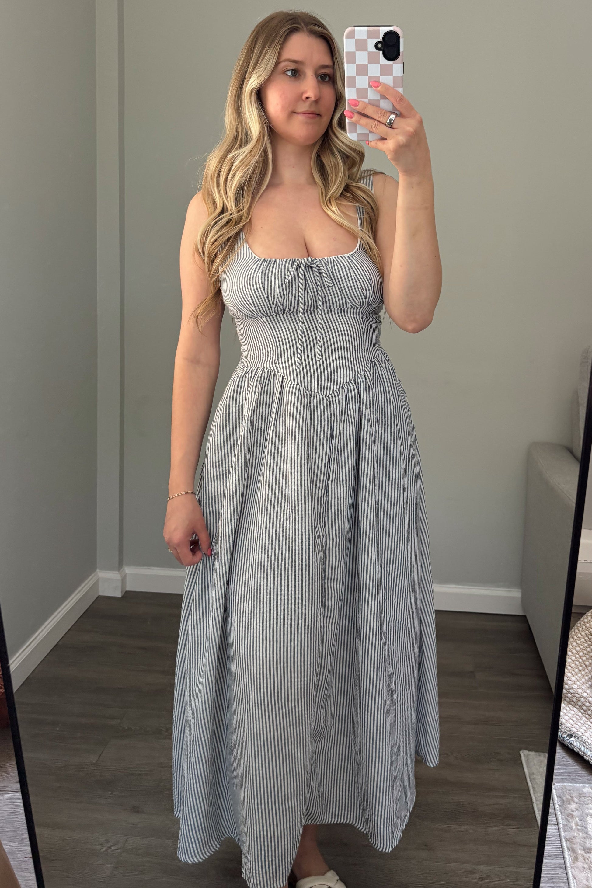 Woman taking a mirror selfie wearing a light blue dress in a room with a couch and window.