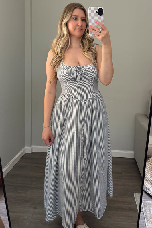 Woman taking a mirror selfie wearing a light blue dress in a room with a couch and window.