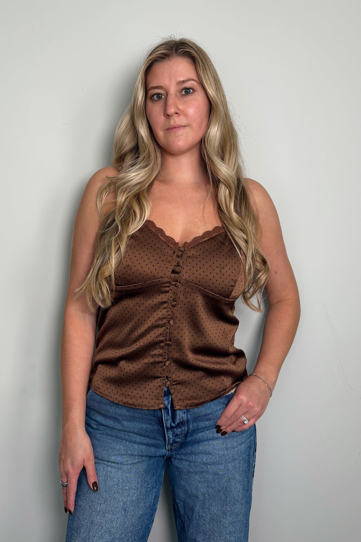 Model wearing the Delancey Polka Dot Cami in brown, a satin button-front cami with a lace-trim v-neckline, styled with blue jeans